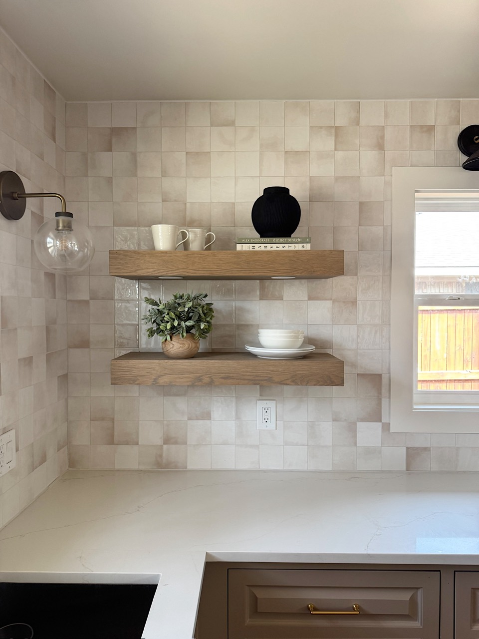 Kitchen detail with floating wood shelves, varied tile, and a light stone countertop