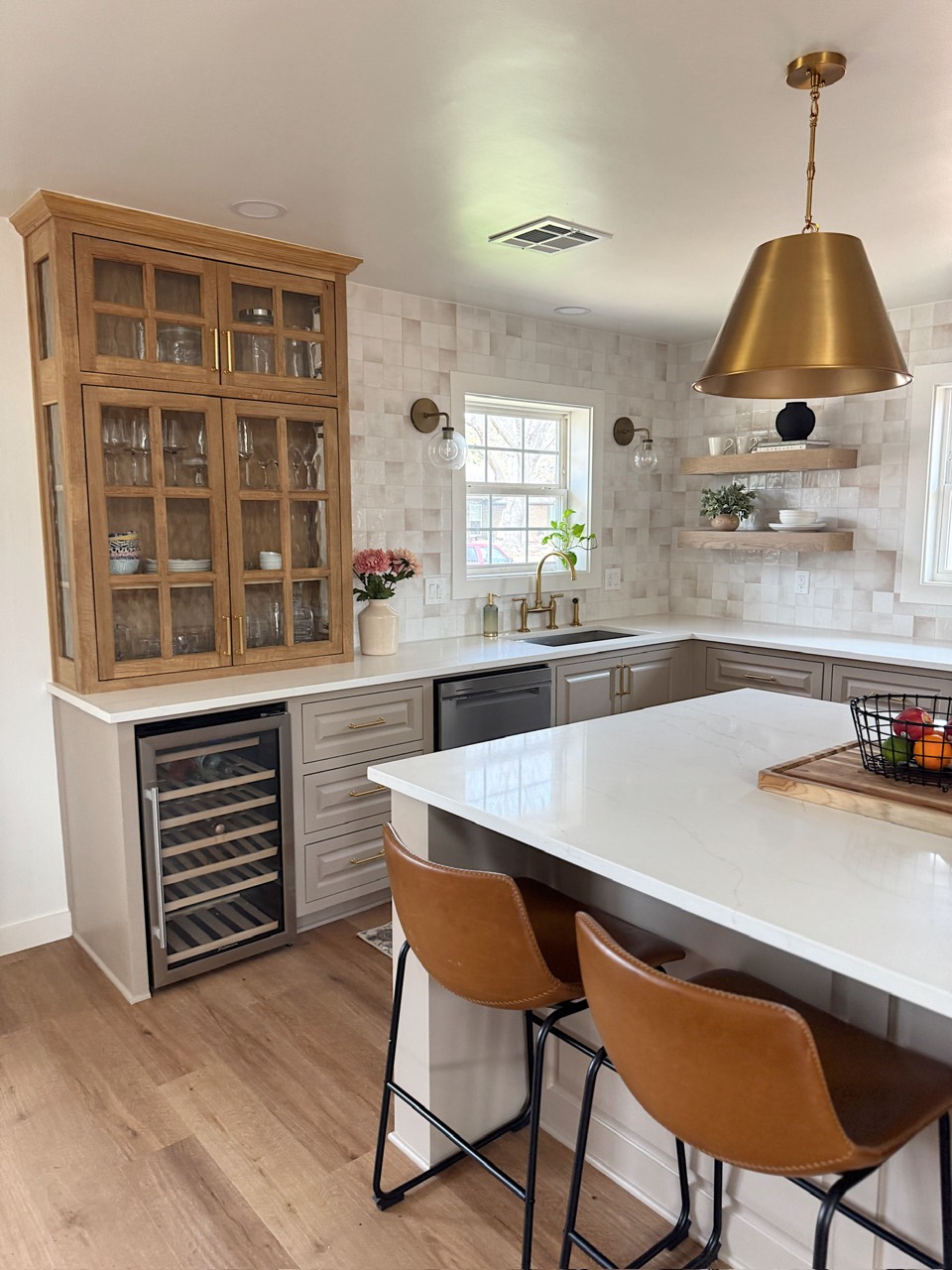 Completed kitchen with warm wood display cabinetry, light tile, a large island, and brass lighting